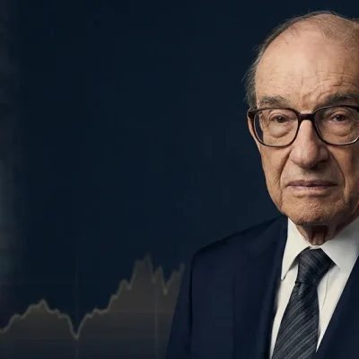 Portrait of Alan Greenspan, former Federal Reserve chairman, against a dark backdrop with a faded classical government building and a stock ticker