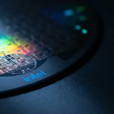 Extreme macro of a silicon semiconductor wafer showing iridescent die grid, with the Intel logo printed on the dark wafer carrier frame