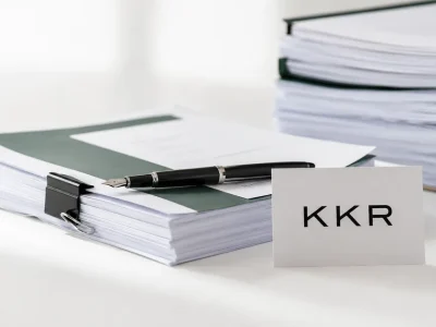 A printed card bearing the KKR logo standing beside bound stacks of legal filing documents and a fountain pen on a white studio backdrop