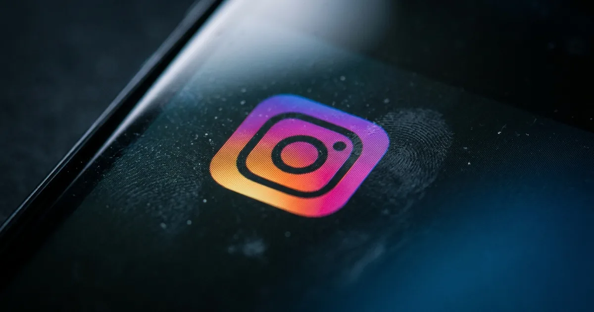 Extreme close-up of the Instagram icon glowing on a dark smartphone screen, with a fingerprint smudge and dust visible on the glass beside it