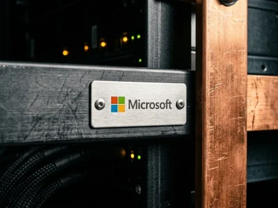 Macro photograph of a brushed steel plate bearing the Microsoft logo riveted to a dark server rail beside a copper power busbar inside a data center rack