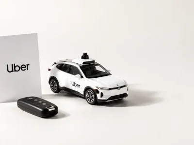 White studio still life with an Uber branded card, a car key fob and a model autonomous vehicle with roof lidar