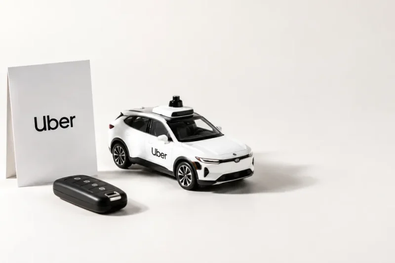 White studio still life with an Uber branded card, a car key fob and a model autonomous vehicle with roof lidar