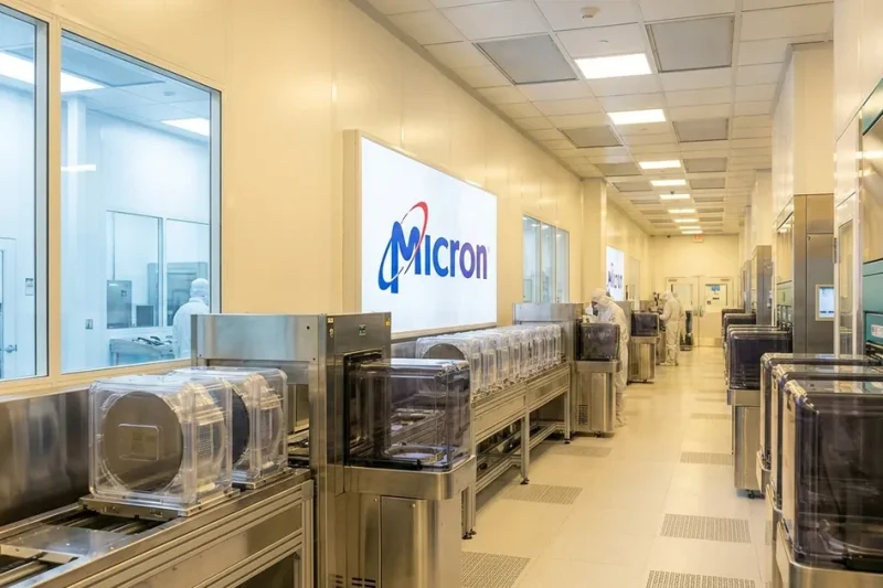 Micron Technology logo on a wall inside a semiconductor cleanroom lined with wafer carriers