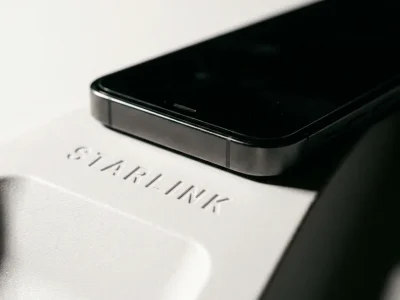 Macro photograph of a black smartphone resting on the white surface of a Starlink satellite dish with the embossed Starlink wordmark in focus