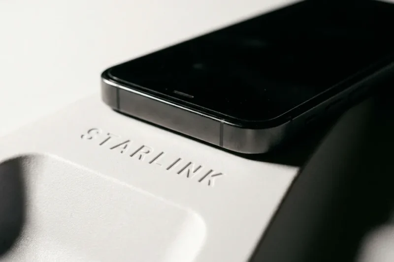 Macro photograph of a black smartphone resting on the white surface of a Starlink satellite dish with the embossed Starlink wordmark in focus