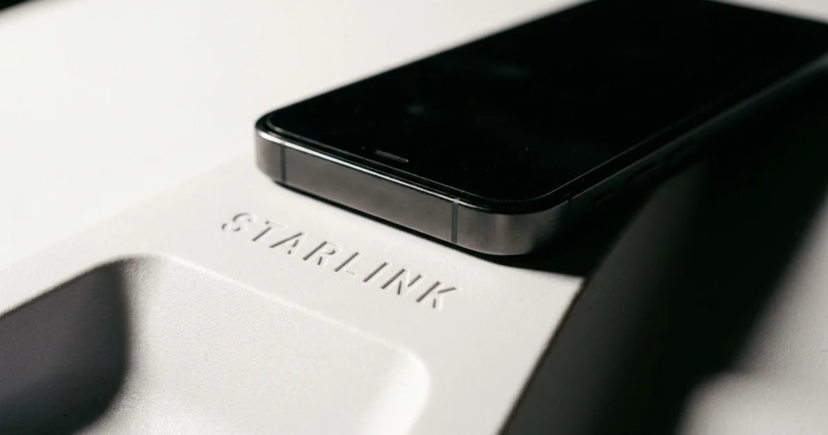 Macro photograph of a black smartphone resting on the white surface of a Starlink satellite dish with the embossed Starlink wordmark in focus